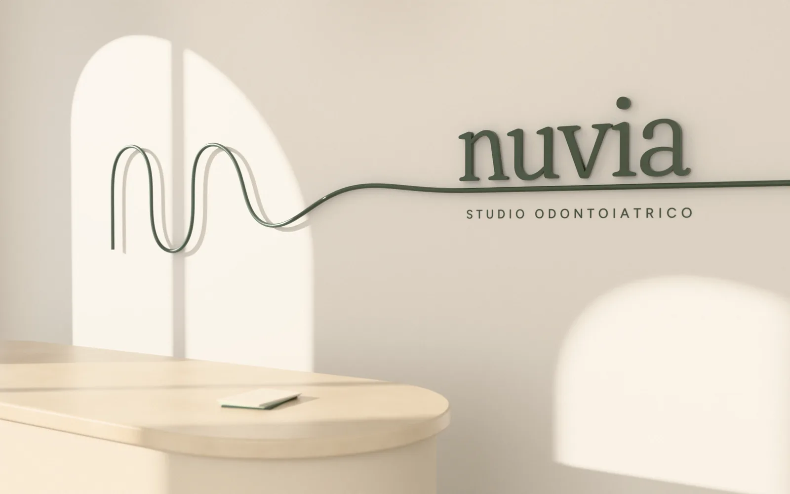 Parete dell’accoglienza dello studio Nuvia: una linea in metallo verde salvia disegna la N del marchio, si distende e diventa la linea di base del logotipo nuvia, con la luce di due finestre ad arco sul muro chiaro