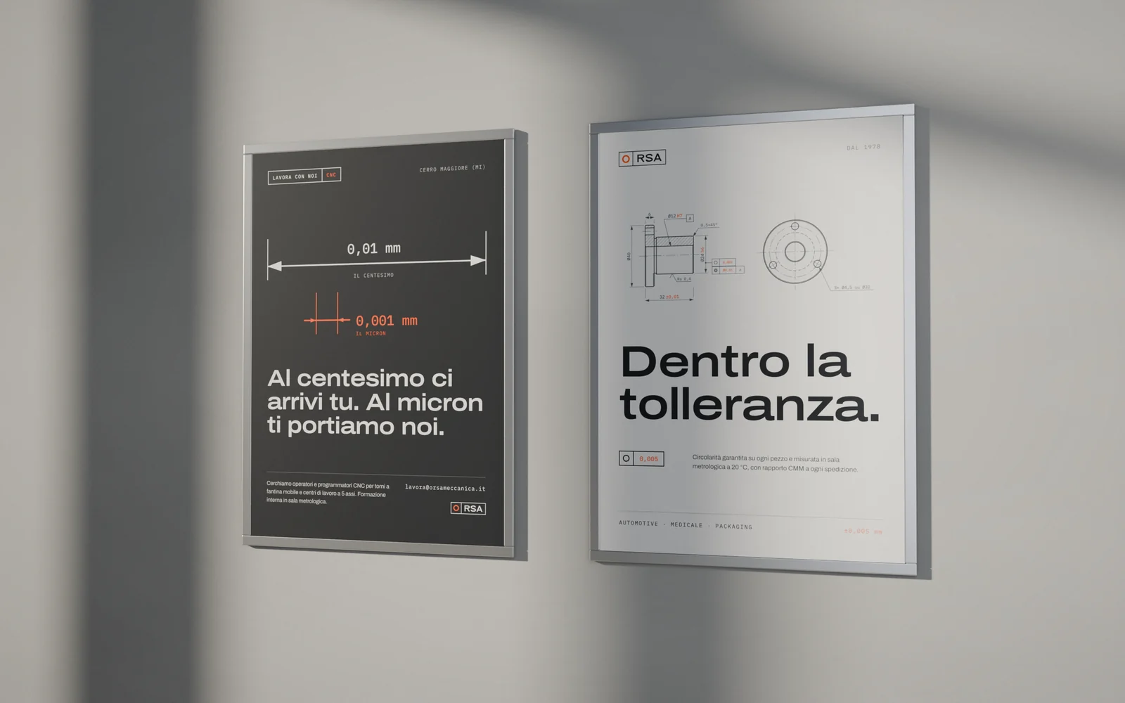 Due manifesti in cornice di alluminio su un muro di cemento in luce radente: campagna recruiting per operatori CNC con le quote di un centesimo e di un micron, e manifesto istituzionale Dentro la tolleranza